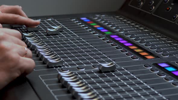 Man Works on a Professional Electronic Audio Mixer. A Control Panel for Tuning Sound Channels