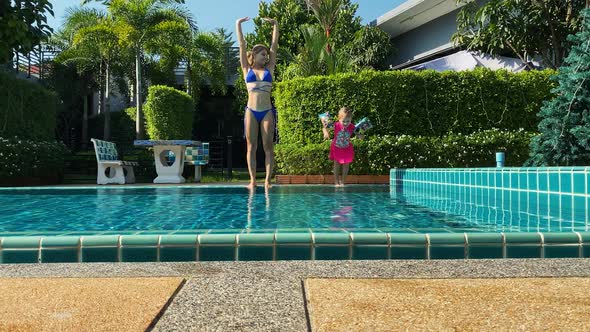 Young Mother and Daughter are Standing on the Edge of the Pool and Jumping Into Water Together