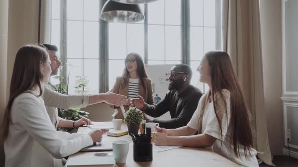 Congratulations with your Promotion! Two Men Shaking Hands and Smiling While Their Coworkers Sitting