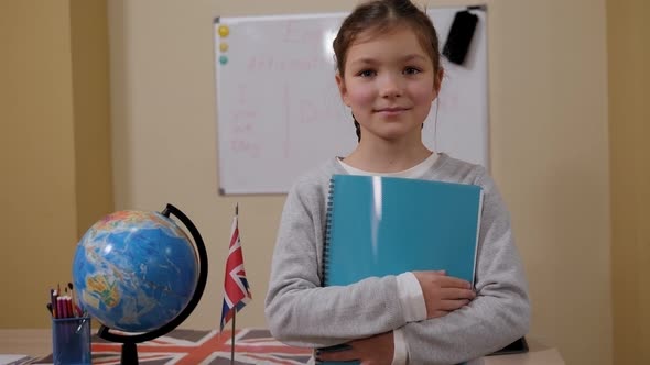 Portrait of Schoolgirl with a Notebook at School Near the Blackboard and a Globe