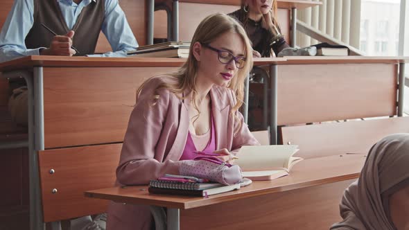 Beautiful Female Student by Desk Listening to Teacher