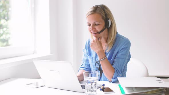 Businesswoman sitting at desk using headset and laptop