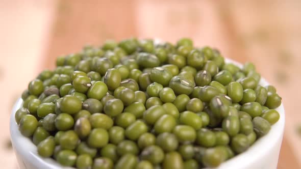 A full white bowl of dry uncooked green mung beans. Falling on a heap in slow motion