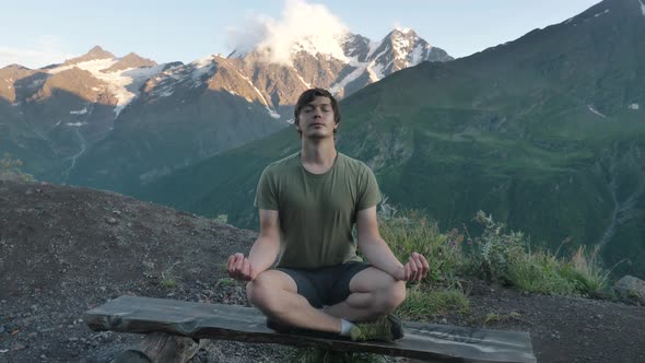 Man Meditates Sitting in Lotus Pose on Wooden Board Bench