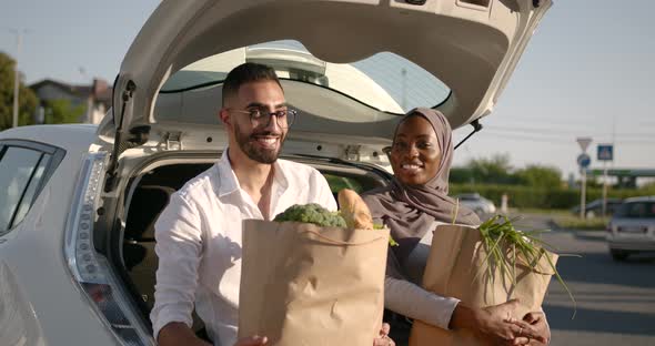 Diverse Couple with Grocery in Paper Bags at Car Trunk