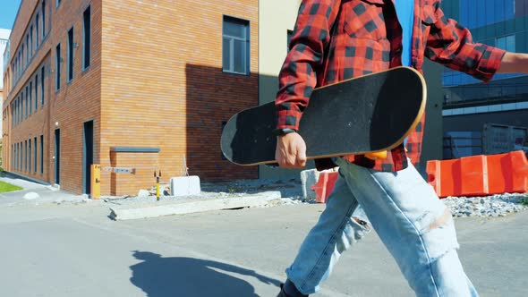 A Young Man Walking Around the City with a Skateboard