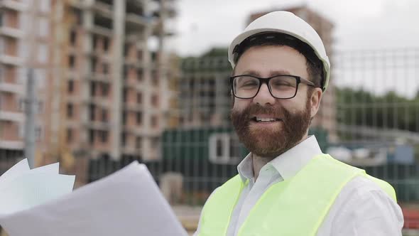 Portrait of a Successful Young Engineer or Architect Wearing a White Helmet, Holding Construction