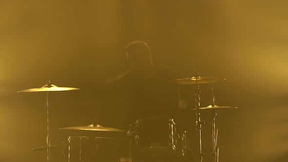Silhouette Drummer Playing on Drum Kit on Stage in a Dark Studio with Smoke and Neon Lighting