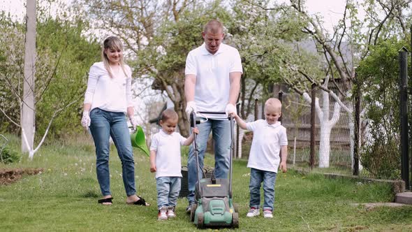 Family Using Lawn-mower and Cutting Grass Together in Village