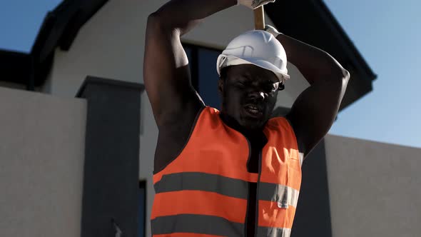 Muscular black male builder swinging a hammer at a construction site