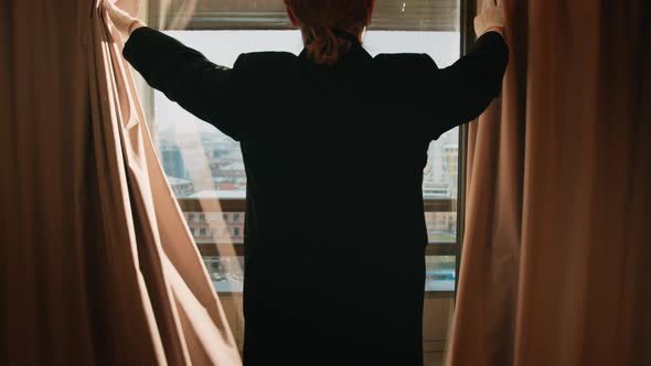 Man in a tuxedo opening the window in a hotel room