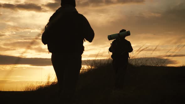 Silhouettes of Two Hikers with Backpacks Enjoying Sunset View From Top of a Mountain. Enjoying the