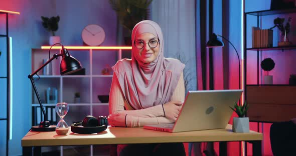 Arabian Girl in Headscarf Sitting at Her Workplace at Home in the Evening and Looking at Camera