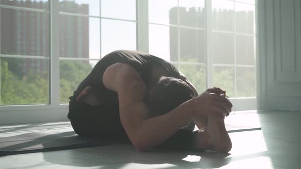 Young Man Doing Yoga in a White Room Filled with Light the Man Does Stretching of the Muscles Near