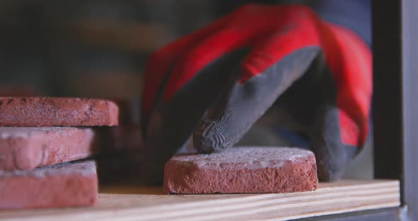 Craftsman in Rubber Work Gloves Carefully Puts Tile Imitating Old Bricks on Shelf of Rack in