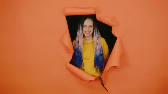 Young Woman Looking Out of Hole of Orange Background and Laughing
