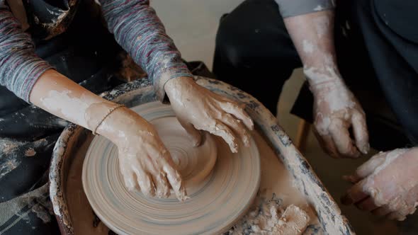 Boy's Hands Making Bowl From Clay Working with Spinning Wheel Under Adult Supervision