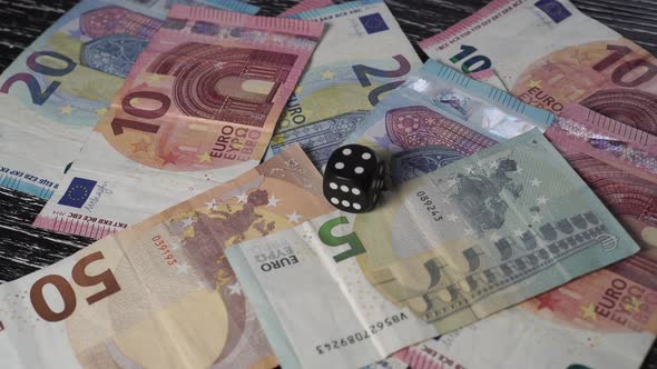 On a pile of euro banknotes, a hand lays a black dice with the number 4 on top. 