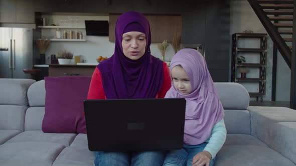 Pretty Muslim Mother with Cute Preschool Daughter in Hijab Sharing Laptop Pc at Home