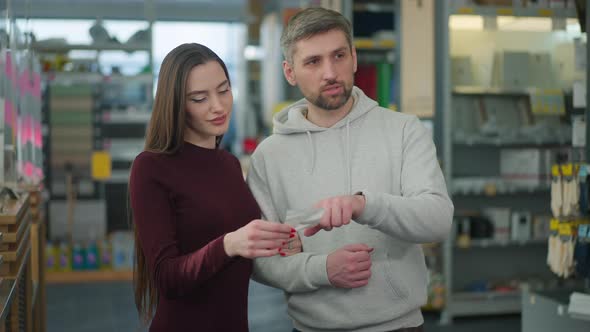 Confident Handsome Caucasian Man Leading Beautiful Slim Woman in Hardware Store