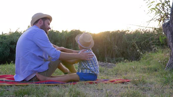 Family Holiday in Open Air, Father with Son Rest on Blanket on Background of Sunset in Rural