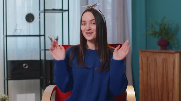 Young Woman Smiling Friendly at Camera Waving Hands Gesturing Hello Hi Greeting at Home on Chair