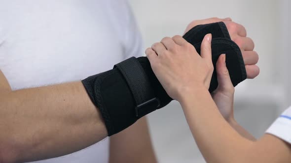 Female Orthopedic Wearing Wrist Support to Male Patient, Trauma Treatment