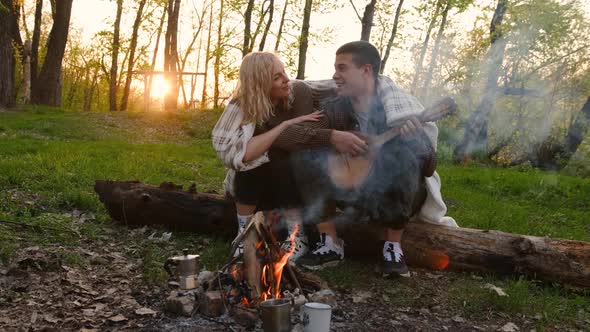 Closeup portrait of a couple sitting with guitar near bonfire in the forest