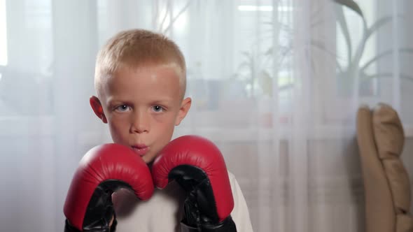 A Small Sevenyearold Boy in Boxing Gloves Practices Punches at Home