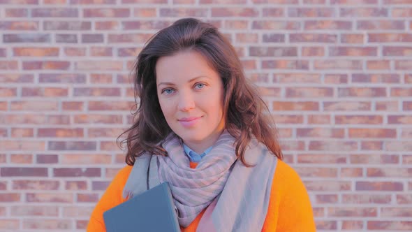 Portrait of a Smiling Woman Freelancer with a Laptop Near Brick Wall
