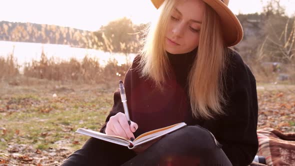 Slow Motion Caucasian Blonde Woman with Beige Hat in Black Sweater Write on Notebook in the