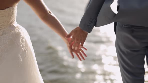Newlyweds Are Standing By the Sea. They Give Each Other Hands. Groom and Bride