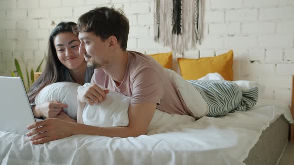 Girl and Guy Wearing Pajamas Using Laptop Computer and Chatting Having Fun in Bedroom in Bed