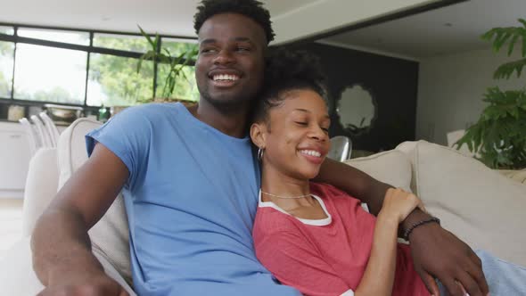 Video of happy african american couple sitting on sofa and embracing