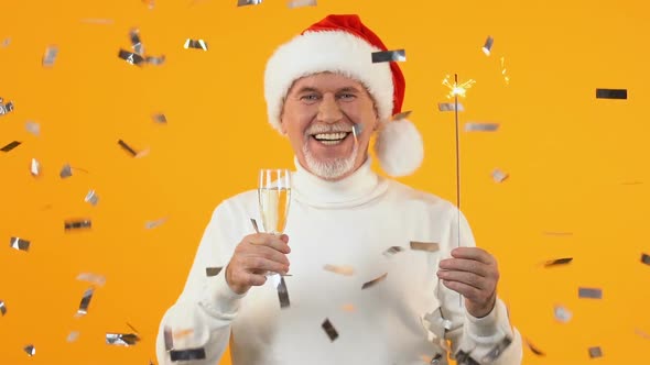 Cheerful Mature Man in Santa Hat Holding Wine Glass and Bengal Light, New Year