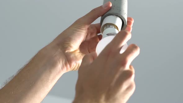 Male hands screwing electricity bulb into switch lampholder