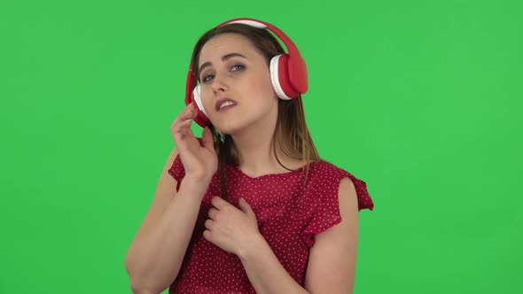 Portrait of Tender Girl in Red Dress Is Dancing and Enjoying Music in Big Red Headphones. Green