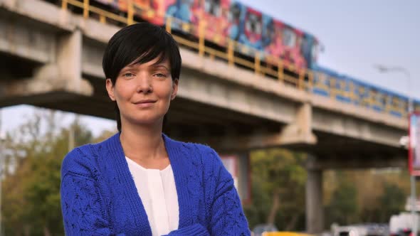 A European Girl Stands Near the Metro Station, Smiles and Looks Into the Camera, Behind the Train