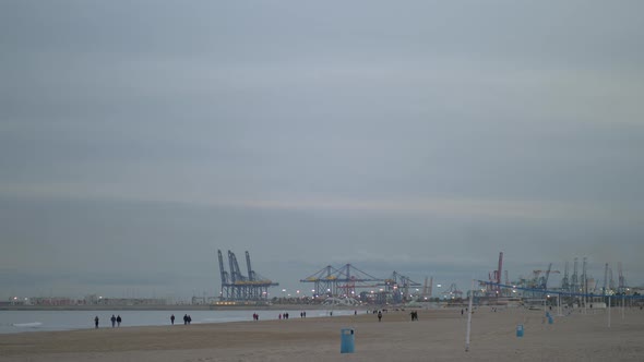 Coast with walking people and container cranes in winter Valencia, Spain