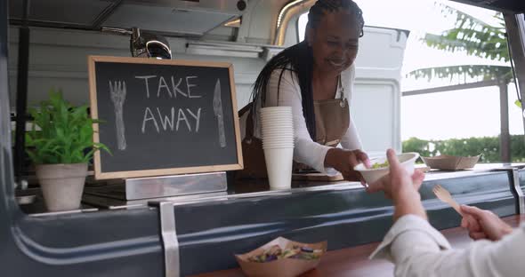 African woman serving takeaway food with eco paper boxes inside food truck