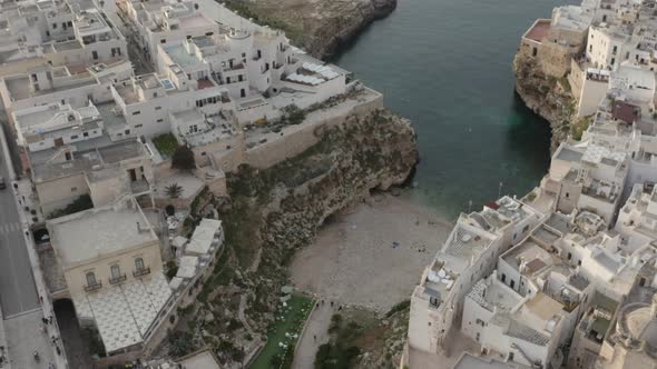 Aerial circle view of beach embedded in the city with people swimming in crystal sea. Polignano a Ma