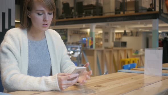 Displeased Woman Using Smartphone in Cafe