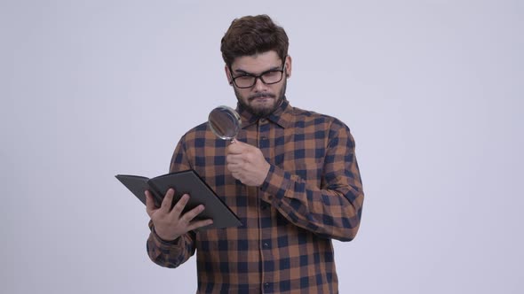 Happy Young Bearded Indian Hipster Man Reading Book with Magnifying Glass