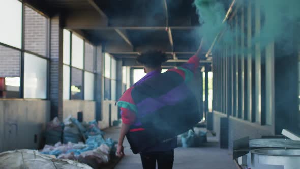 Mixed race man holding blue flare running through an empty building