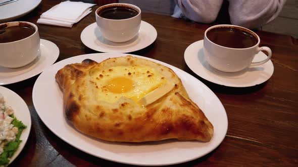 Adjarian Khachapuri on a Table in a Georgian Restaurant Next To Salad, Omelette and Coffee