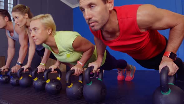 Group of people performing push-up with kettlebell