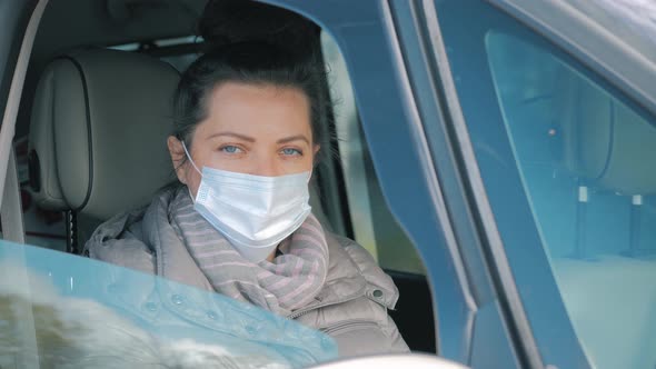 Woman in Car with Surgical Mask on Face Opening Car Window