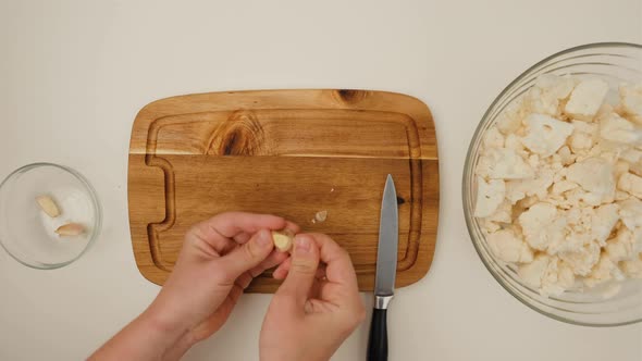 Top view of woman hands with knife cutting garlic for salad on a wooden board.
