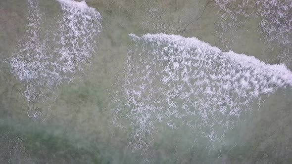 Bird's eye aerial drone view of waves in shallow water off the coast of the small town of Matutinao