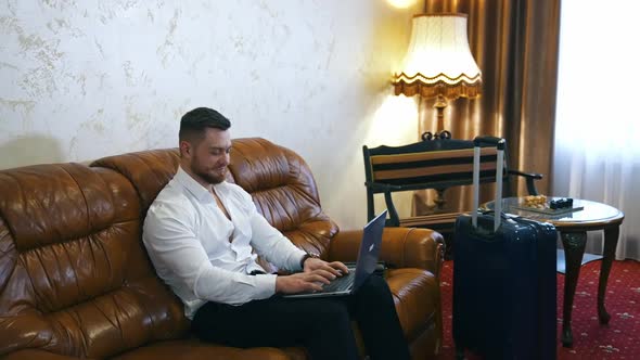 Handsome young businessman works on laptop in a hotel room